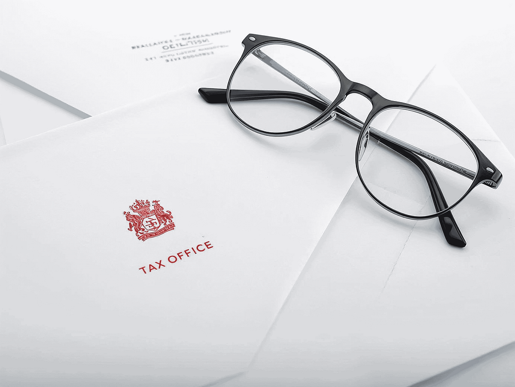 Skutki braku meldunku w Holandii – wezwania i kary finansowe. Oficjalne pismo z holenderskiego urzędu skarbowego Tax Office i okulary leżące na białej kopercie.