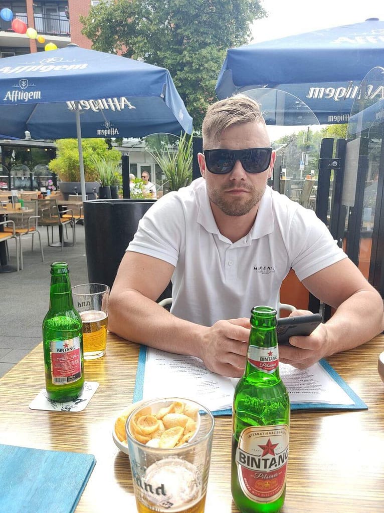 Założyciel portalu Pomocnik Holenderski siedzący w letnim ogródku restauracyjnym przy stoliku z napojami.