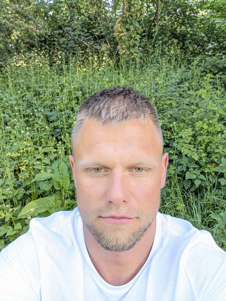 Portret założyciela portalu Pomocnik Holenderski na tle zielonej roślinności.