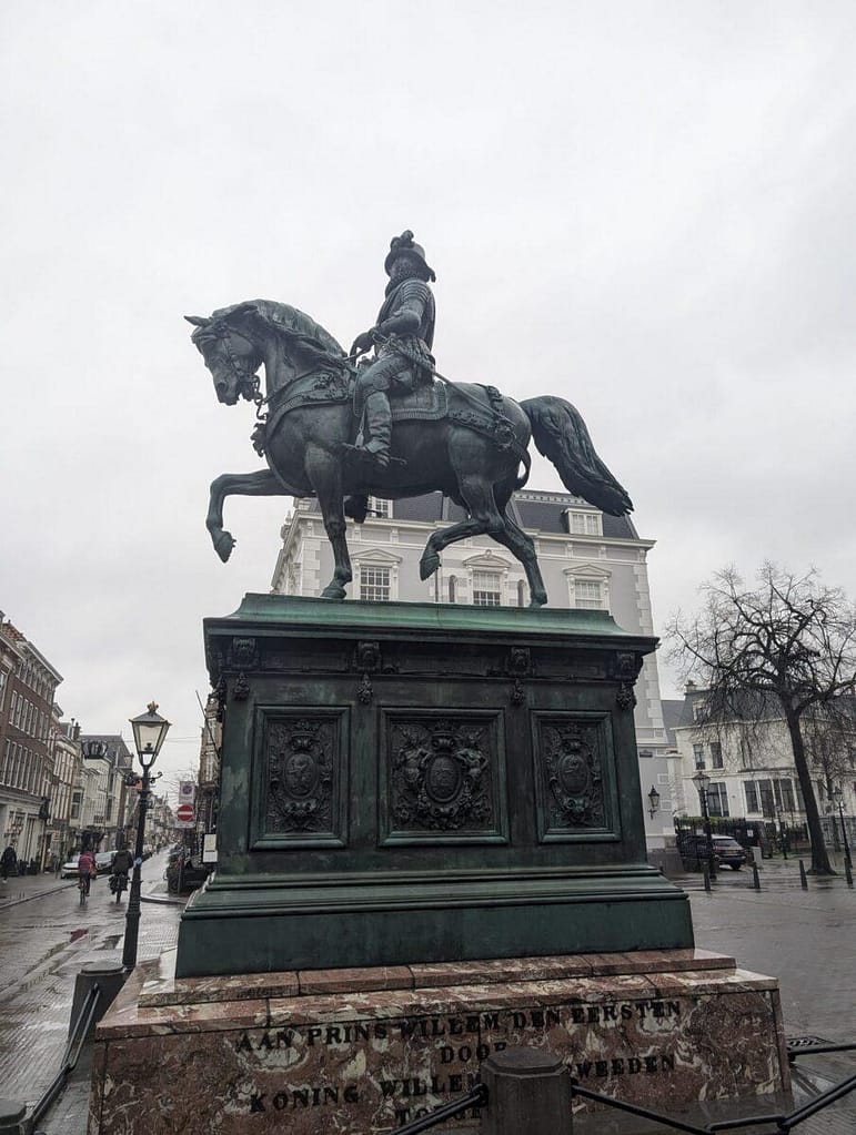 Historyczny pomnik konny Wilhelma I Orańskiego na placu w Hadze na tle klasycystycznej kamienicy.